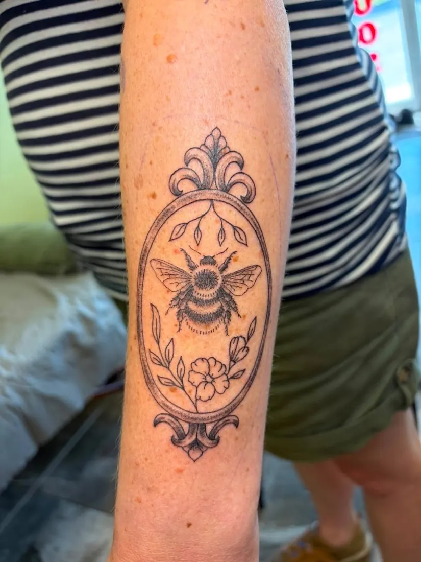 Fine-line bee in an oval frame on an upper arm