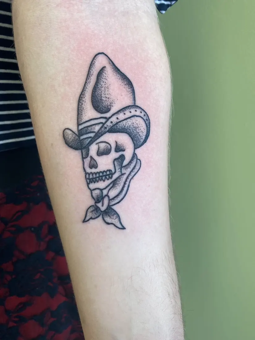 Traditional skull in a cowboy hat tattoo on a forearm