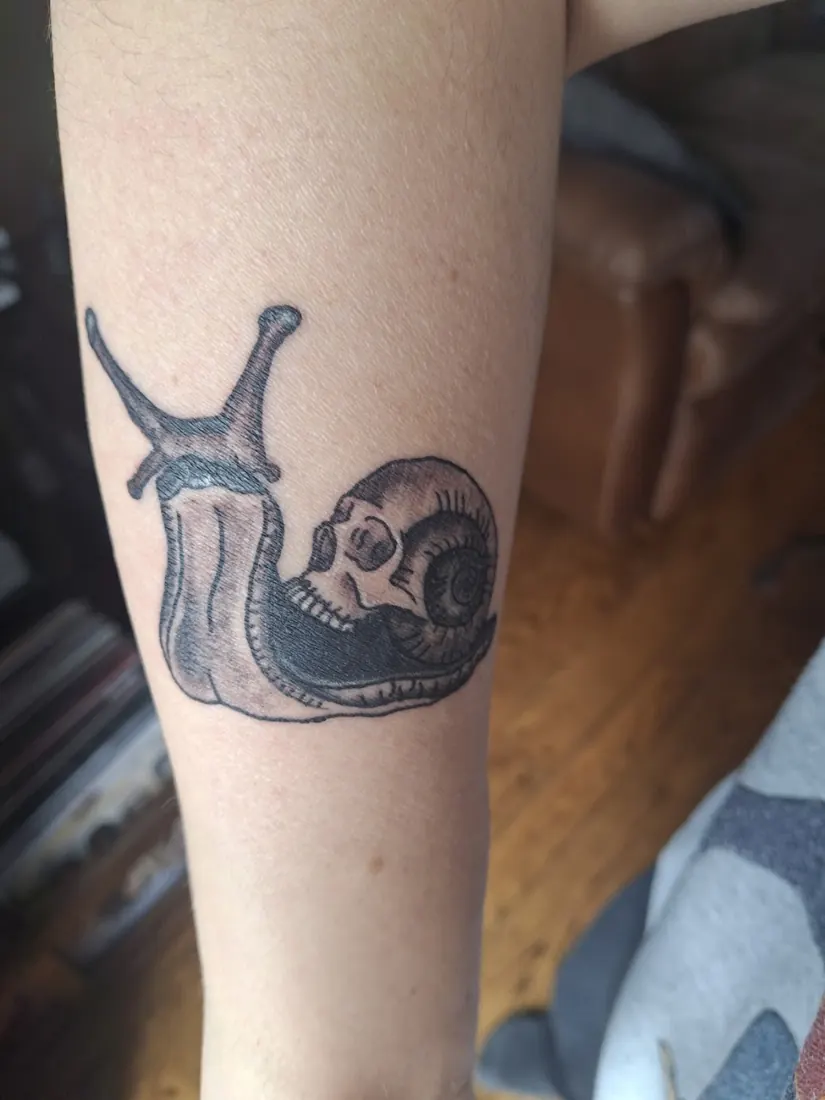 Black-and-grey snail with a skull shell tattoo on a calf
