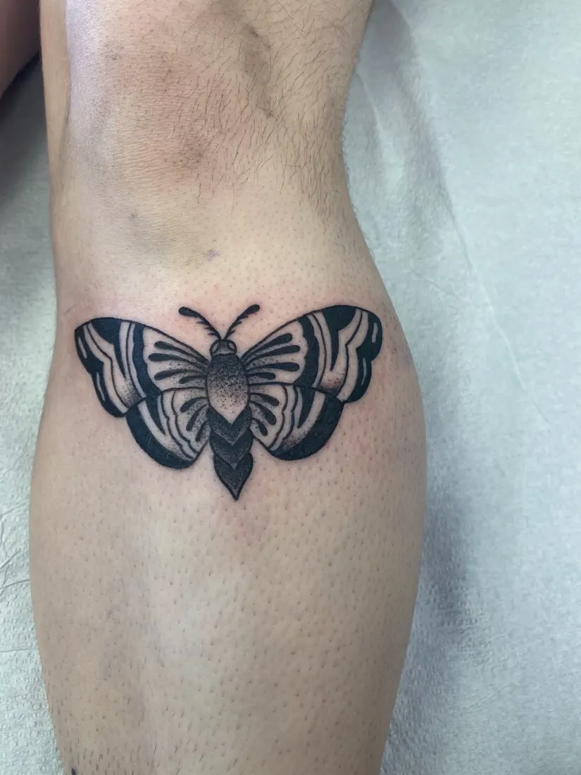 Black moth tattoo on a lower leg